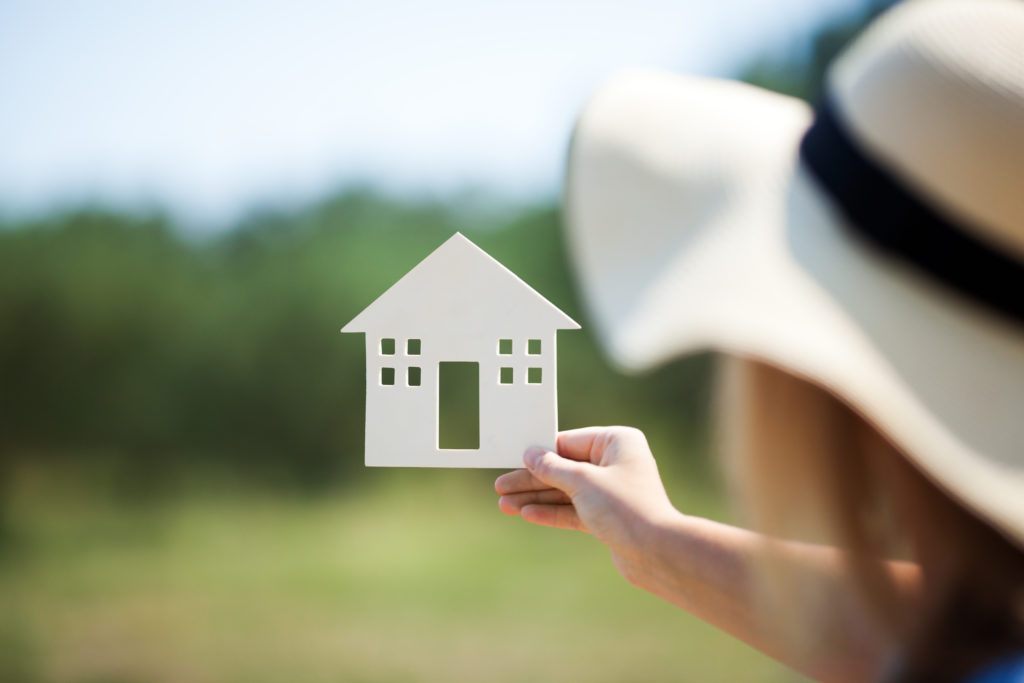 Woman in summer hat holding small house model outdoor.